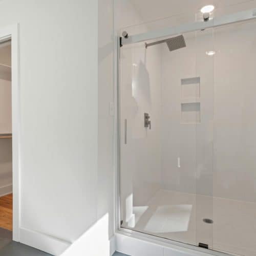 Bright minimalist bathroom interior featuring a glass shower enclosure with sleek design.
